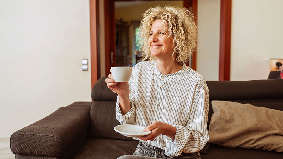 woman sat on sofa with cup of tea wondering "what are the benefits of vision correction"