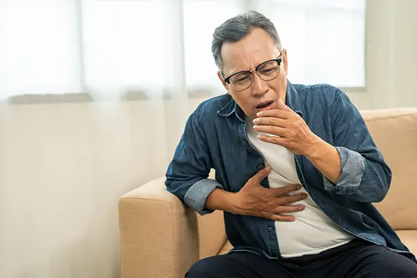 Man wearing glasses sitting down coughing.