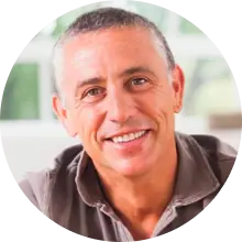 A portrait image of man who is wearing a brown shirt smiling at the camera.